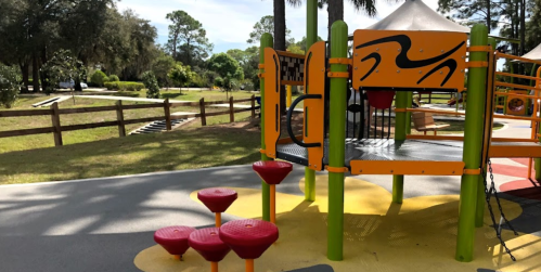 Colorful playground equipment with climbing structures and steps, set in a green park with trees in the background.
