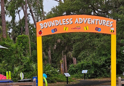 Colorful sign reading "Boundless Adventures" surrounded by greenery and trees, with playful decorations.