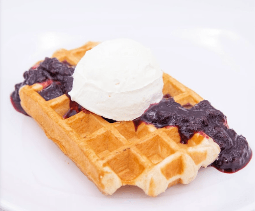 A golden waffle topped with a scoop of vanilla ice cream and drizzled with berry sauce.