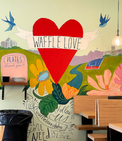 Colorful mural featuring a large heart, flowers, and the text "Waffle Love" in a cozy café setting.