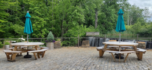Outdoor seating area with wooden tables and teal umbrellas, overlooking a small waterfall and lush greenery.
