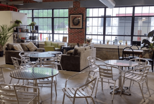 Cozy café interior with sofas, tables, and plants, featuring large windows and a warm, inviting atmosphere.