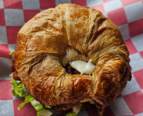 A croissant sandwich filled with lettuce, bacon, and mayonnaise, served in a red and white checkered paper.