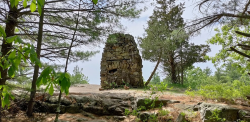 A stone structure surrounded by trees on a rocky terrain, with greenery in the background under a clear sky.