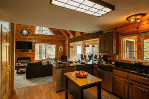 Cozy wooden kitchen with a central island, large windows, and a living area featuring a sofa and TV.