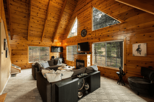 Cozy wooden cabin living room with high ceilings, large windows, and a comfortable seating area.