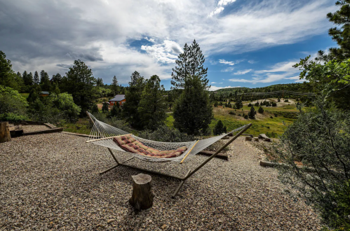 A hammock on a gravel patio overlooks a scenic landscape of trees and rolling hills under a cloudy sky.