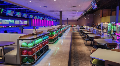 A vibrant bowling alley with colorful bowling balls, seating areas, and arcade games under bright lights.