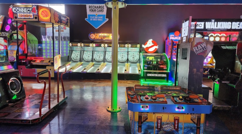 A vibrant arcade featuring various games, including skee-ball, a Ghostbusters machine, and a Connect 4 game.