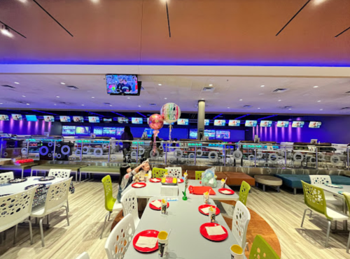 A vibrant bowling alley with colorful decor, tables set for dining, and bowling lanes in the background.