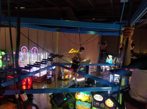 A view from above an arcade, showing people on a ropes course with colorful games below.