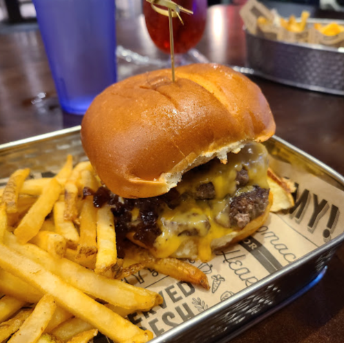 A juicy cheeseburger with melted cheese and a skewer, served with crispy French fries on a metal tray.