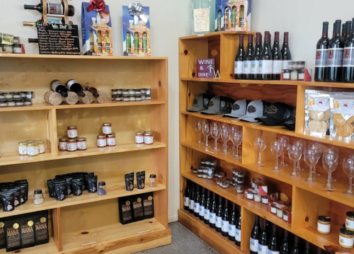 A cozy shop display featuring shelves of wine, jars, snacks, glasses, and merchandise.