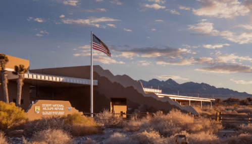 Desert National Wildlife Refuge building with American flag, surrounded by desert landscape and mountains in the background.
