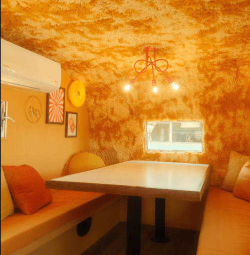 Cozy interior of a small space with orange shag walls, a table, and seating, illuminated by a unique light fixture.