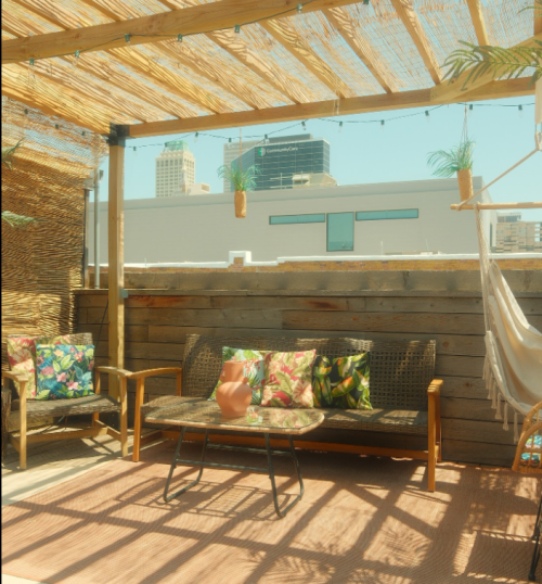 A cozy outdoor seating area with a table, colorful cushions, and a hammock, surrounded by city buildings.