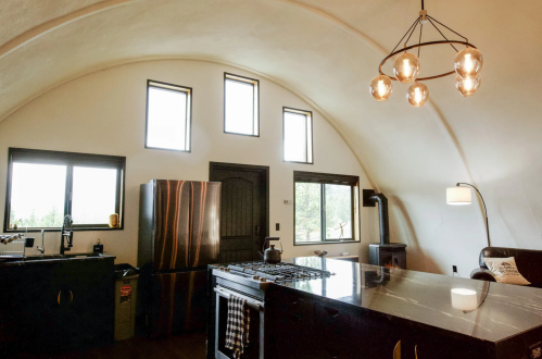 Modern kitchen with curved ceiling, large windows, stainless steel appliances, and a stylish light fixture.