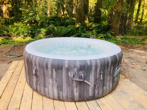 An inflatable hot tub on a wooden deck, surrounded by lush greenery in a forested area.