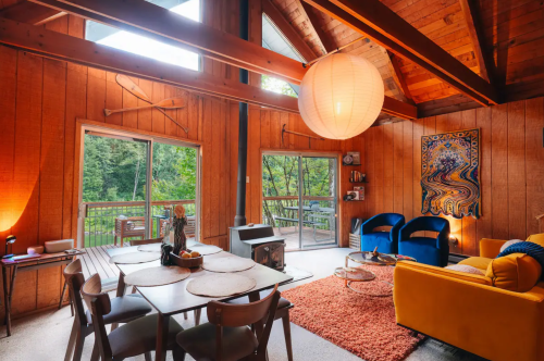 Cozy cabin interior with wooden walls, large windows, colorful furniture, and a warm atmosphere.