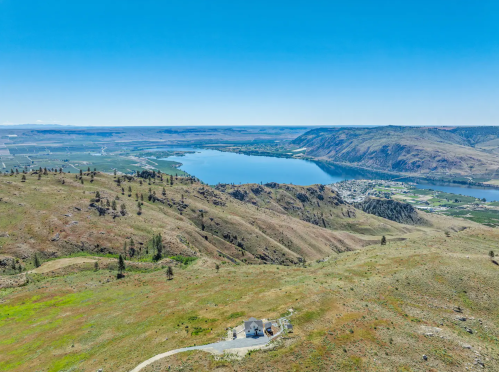 Aerial view of a serene landscape featuring rolling hills, a river, and a small house near the water's edge.