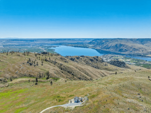 Aerial view of a serene landscape featuring rolling hills, a river, and a small house near the water's edge.