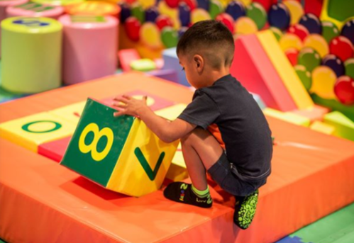 A child plays with large colorful foam blocks in a vibrant indoor play area.
