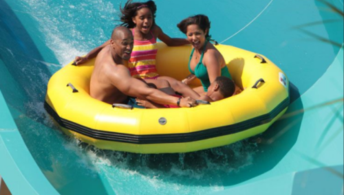 A family of four enjoys a water slide in a yellow inflatable raft, splashing down with excitement.