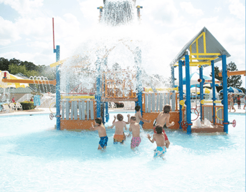 Children playing in a splash pad, enjoying water features and a sunny day at a water park.