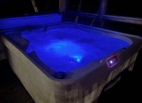 A hot tub with glowing blue water, illuminated in a dimly lit outdoor setting.