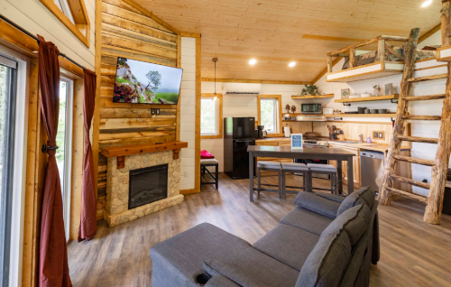 Cozy cabin interior featuring a living area, kitchen, and rustic decor with a fireplace and wooden accents.