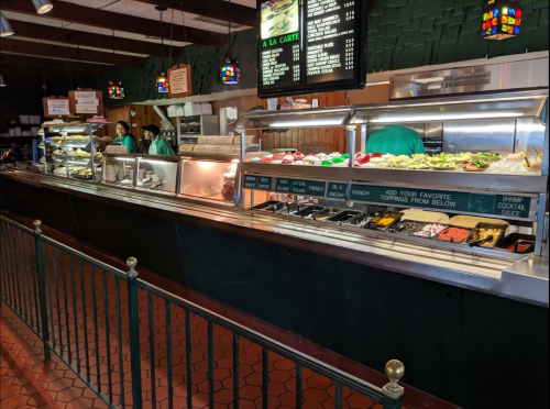 A buffet counter with various food options, including salads and toppings, in a casual dining setting.