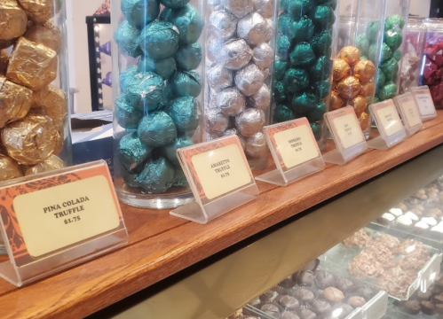 A display of assorted truffles in jars, labeled with prices, including Piña Colada and Marzipan varieties.