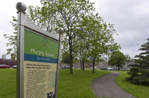 Sign for Murphy Square park with trees and a pathway in the background, showcasing green grass and a peaceful setting.