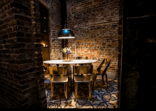 A cozy dining area with a marble table, wooden chairs, and exposed brick walls, illuminated by a pendant light.