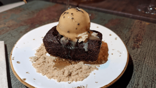 A slice of chocolate cake topped with a scoop of ice cream, drizzled with sauce, and served on a plate with crumbs.