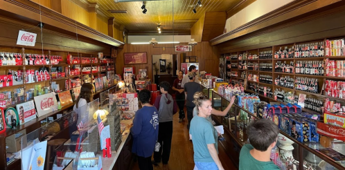 A vintage store filled with Coca-Cola memorabilia, featuring customers browsing shelves lined with colorful products.
