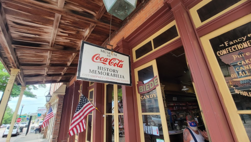 Sign for the Coca-Cola Museum displaying history and memorabilia, with American flags and a candy store visible.