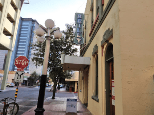A street view of a building with a sign reading "Reilly," featuring a stop sign and a nearby open sign.