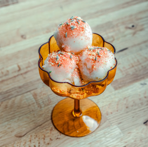 Three scoops of ice cream topped with sprinkles in a vintage amber glass dish on a wooden table.