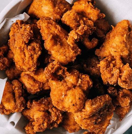 A close-up of a basket filled with crispy, golden-brown fried chicken pieces.