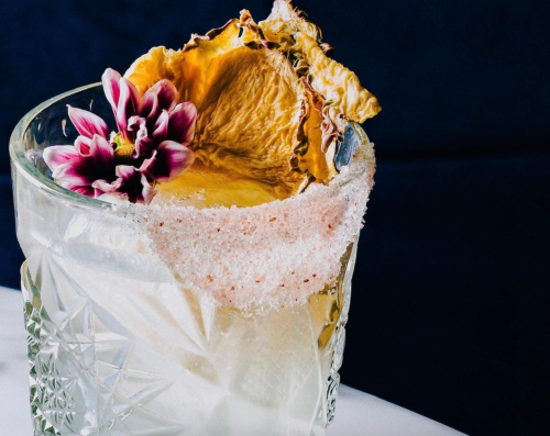 A beautifully garnished cocktail with a dried pineapple slice and a flower, served in a textured glass.