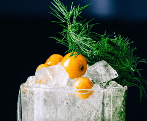 A refreshing cocktail with ice, garnished with green herbs and yellow fruit.