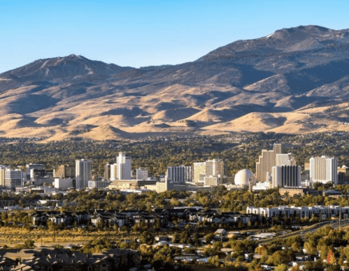 A panoramic view of a city skyline with mountains in the background and clear blue skies.