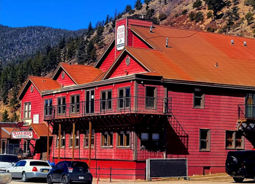 A red wooden building with a sign reading "Texas Reds" surrounded by mountains and parked cars.