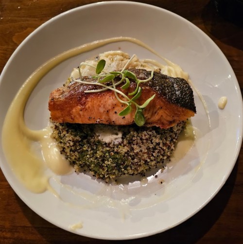 A plate featuring grilled salmon on a bed of quinoa, garnished with microgreens and drizzled with a creamy sauce.