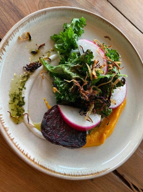 A plate featuring a colorful salad with greens, radishes, beets, and a drizzle of sauce on a rustic wooden table.