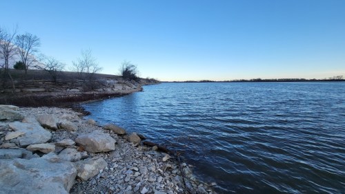 A serene lakeside view with rocky shorelines and clear blue skies reflecting on the water's surface.
