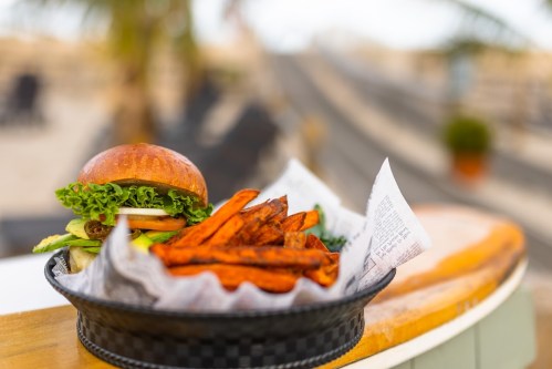 A delicious burger with lettuce and tomato served with a side of crispy sweet potato fries in a basket.