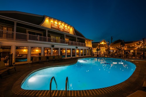 A beautifully lit pool area at dusk, with a charming building and warm lights reflecting on the water.