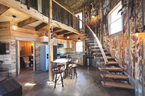 Cozy interior of a rustic cabin featuring a spiral staircase, kitchen, and wooden accents. Natural light from windows.